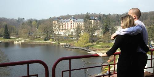 a man and woman standing on a balcony overlooking a lake at Hôtel Spa Du Béryl in Bagnoles de l'Orne