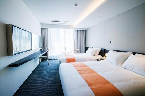 a hotel room with two beds and a television at Gloucester Hotel Jeju in Jeju