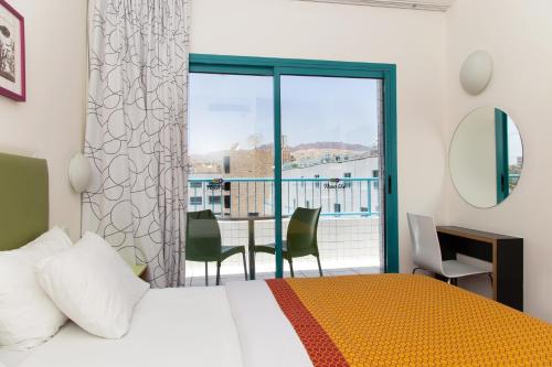 a bedroom with a bed and a balcony with a table and chairs at Nova Like Hotel - an Atlas Hotel in Eilat