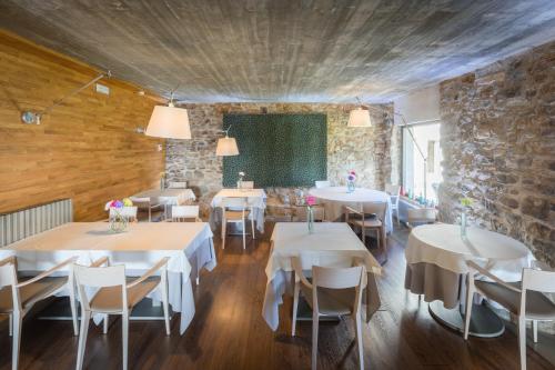restauracja z białymi stołami i krzesłami oraz kamienną ścianą w obiekcie Les Planes del Grau w mieście Sant Joan de les Abadesses