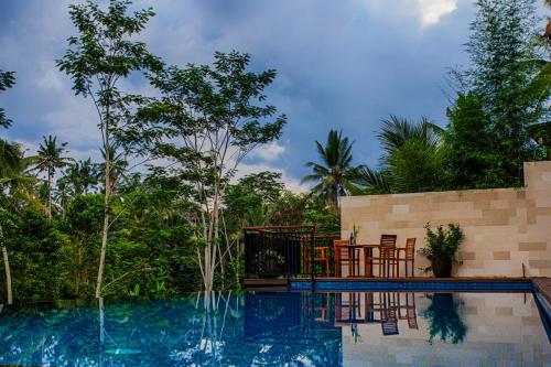 a swimming pool with chairs and a table and trees at River Sakti Ubud by Prasi in Ubud