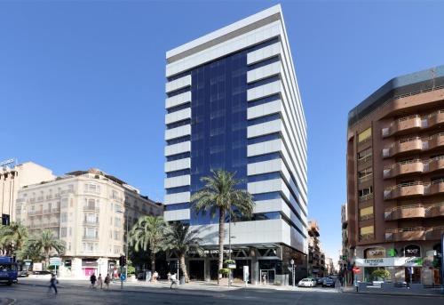 un grand bâtiment dans une rue de la ville bordée de palmiers dans l'établissement Eurostars Lucentum, à Alicante