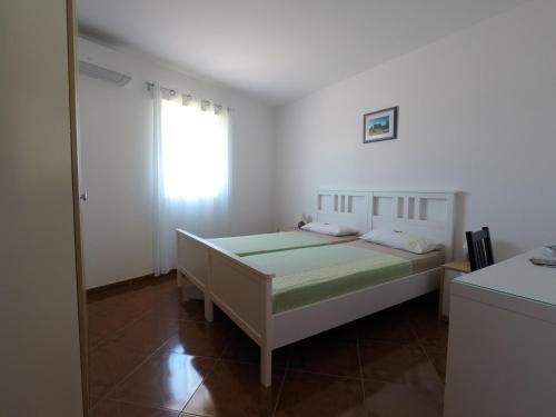 a white bedroom with a bed and a window at Apartments Pegla in Nerezine