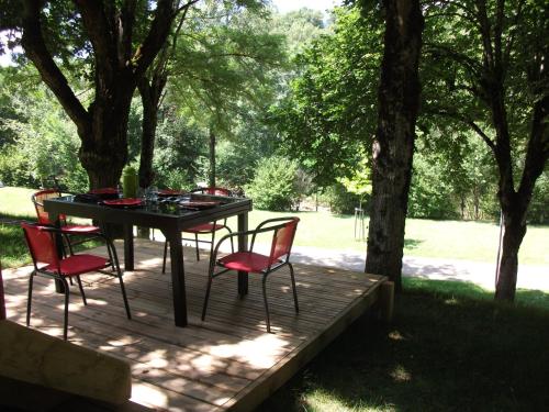 a table and chairs on a wooden deck with trees at Les Cahutes d'Olt in Saint-Laurent-dʼOlt