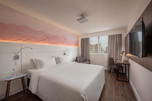 a hotel room with a large white bed and a tv at Intercity Porto Alegre Cidade Baixa in Porto Alegre