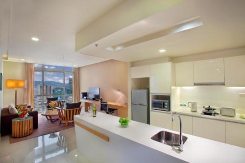 a kitchen with white cabinets and a living room at PARKROYAL Serviced Suites Kuala Lumpur in Kuala Lumpur