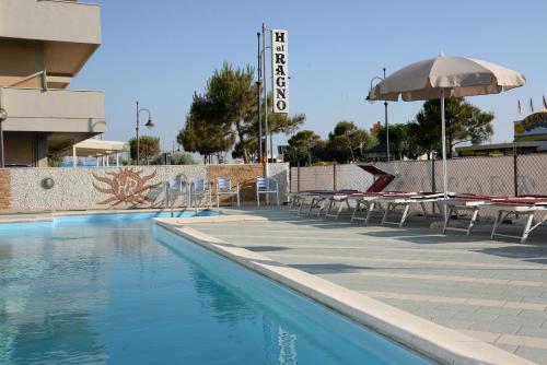 uma piscina com mesas e cadeiras e um guarda-sol em Hotel Al Ragno em Cesenatico