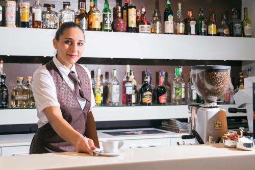 a woman standing behind a bar with a cup of coffee at Hotel La Bussola in Milazzo