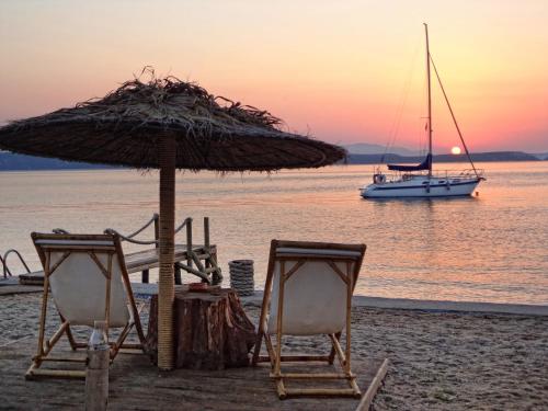 two chairs and an umbrella on a beach with a boat at Venus Beach Hotel in Nea Stira