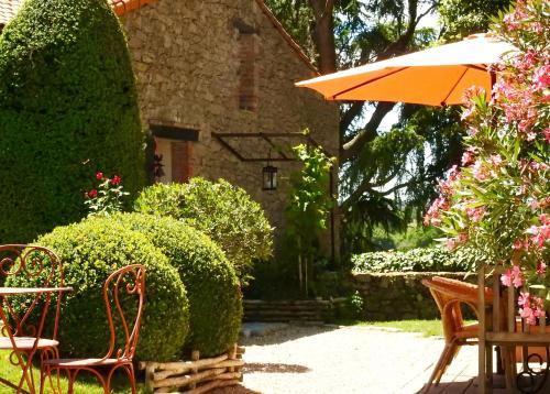 un jardín con sillas, una sombrilla y arbustos en La Blanchisserie en Le Puy-Saint-Bonnet