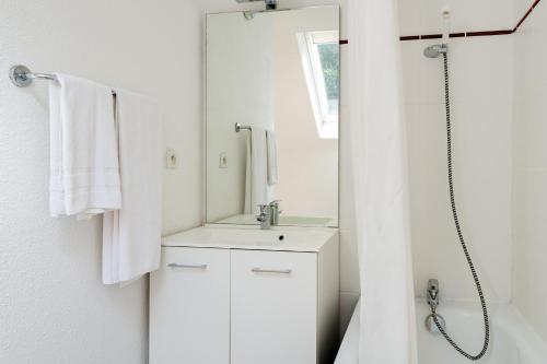 een witte badkamer met een wastafel en een spiegel bij Lagrange Vacances Le Domaine des 100 Lacs in Cauterets