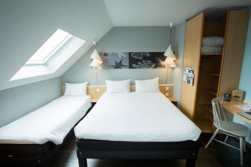 a bedroom with two beds and a desk and a window at ibis Cherbourg La Glacerie in Cherbourg en Cotentin