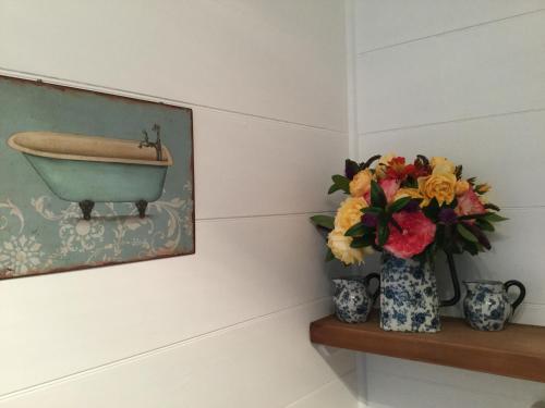 a painting of a bath tub and a vase with flowers on a shelf at The Old School House in Te Awamutu