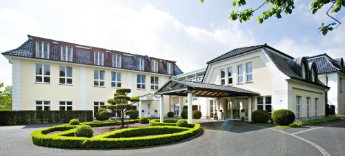 une grande maison blanche avec une cour entourée de buissons dans l'établissement Hotel Sonne, à Rheda-Wiedenbrück
