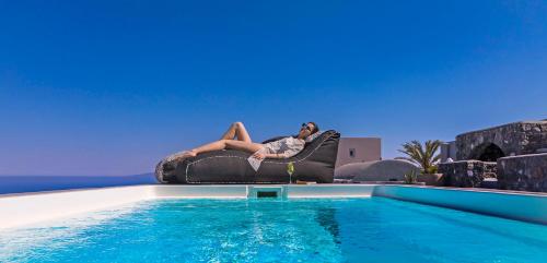 a woman sitting on a chair next to a swimming pool at Elysian Santorini in Oia