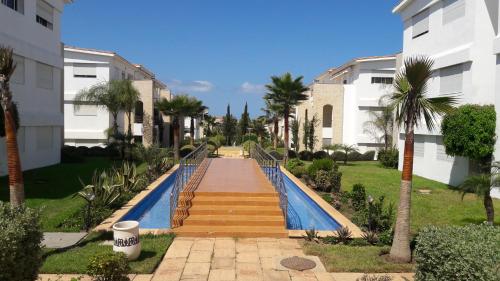 a swimming pool in a yard with palm trees and buildings at Les perles de tamaris dar bouazza in Dar Mohammed Ould Haj Jilali