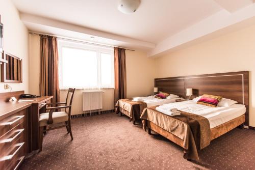 a hotel room with two beds and a desk at Hotel Austeria Conference & Spa in Ciechocinek