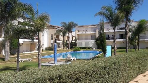 a swimming pool in front of a building with palm trees at Les perles de tamaris dar bouazza in Dar Mohammed Ould Haj Jilali