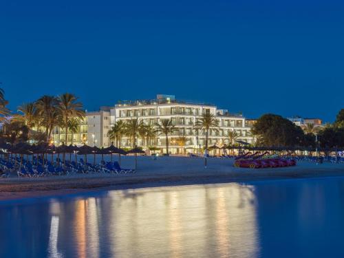a building on a beach with palm trees and the water at H10 Casa del Mar in Santa Ponsa