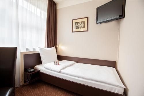 a bed in a hotel room with a tv on the wall at Hotel Diament Spodek in Katowice