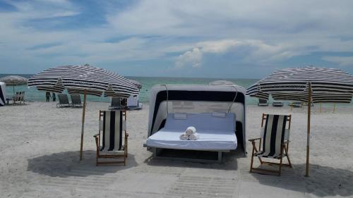 a bed and two chairs on a beach with umbrellas at Zota Beach Resort in Longboat Key
