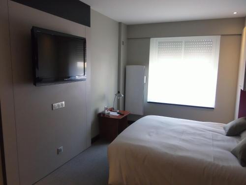 a bedroom with a bed and a tv and a window at The Originals Boutique, Hôtel La Chaussairie, Rennes Sud in Chartres-de-Bretagne