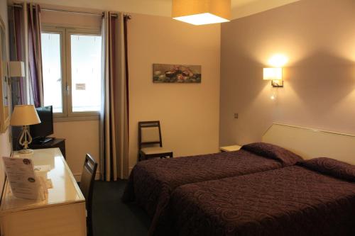 a hotel room with a bed and a desk and a window at Hôtel restaurant LOGIS HOTELLERIE DE BALAJAN in Vic-la-Gardiole