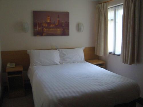 a bedroom with a bed with white sheets and a window at Firs Hotel in Hitchin