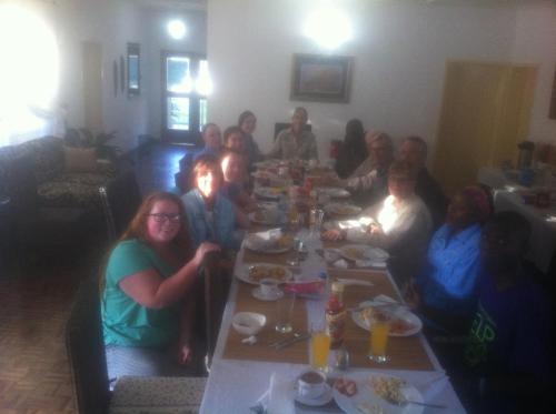 un grupo de personas sentadas en una mesa larga comiendo en Kuku Royal Lodge, en Ndola