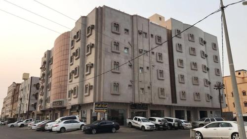 ein großes Gebäude mit Autos auf einem Parkplatz in der Unterkunft منازل الساهر للوحدات السكنية فرع 1 in Al Qunfudhah