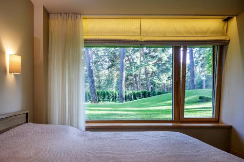 ein Schlafzimmer mit einem Fenster mit Blick auf einen grünen Hof in der Unterkunft Anbo Vila in Palanga