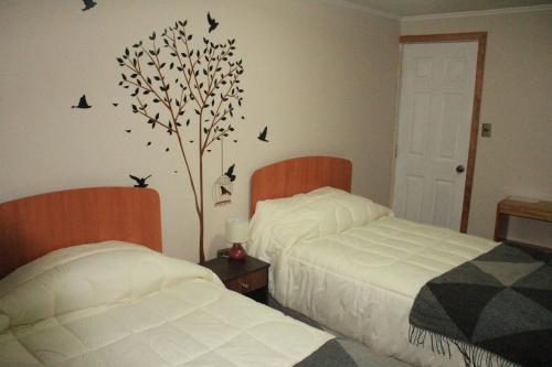 a bedroom with two beds and a tree with birds on the wall at Hostal Los Teros in Coihaique