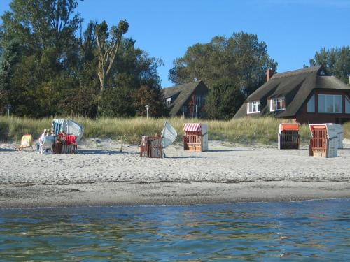 a beach with chairs and a house in the background at Hotel am Wind in Großenbrode