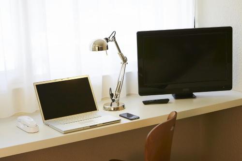 a desk with a computer monitor and a laptop on it at Campanile Hotel Compiegne in Compiègne