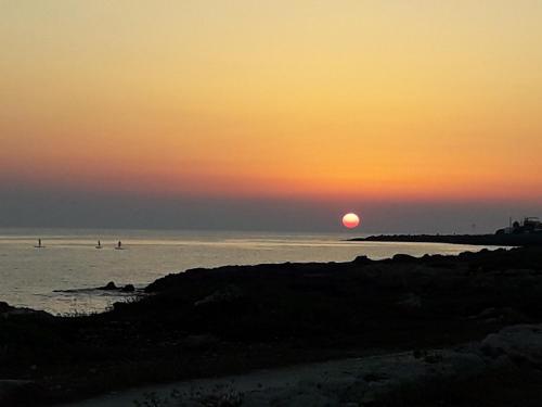 a sunset over the ocean with people in the water at Giardino dei Baroni house in Marina di Mancaversa