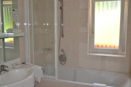 ein Badezimmer mit einer Dusche, einem Waschbecken und einer Badewanne in der Unterkunft Hotel Scoiattolo in Wolkenstein in Gröden