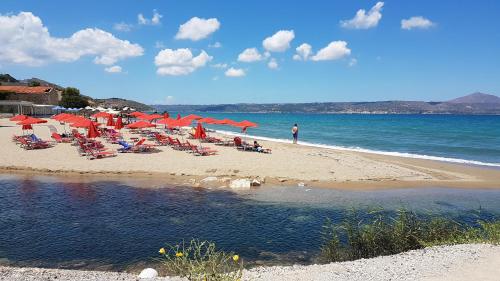 a beach with chairs and red umbrellas and the ocean at Akti Galinis in Kalyves