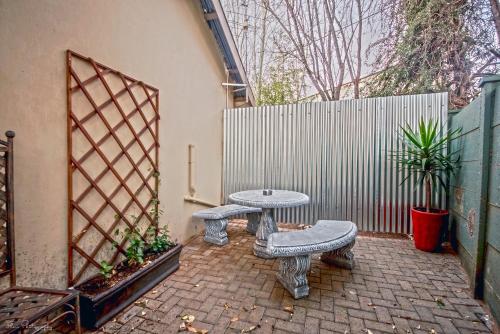 a patio with two benches and a table and a fence at Crisp Guest Rooms in Bloemfontein