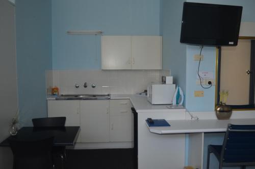 a kitchen with white cabinets and a tv on the wall at Tall Timbers Motel in Dungog
