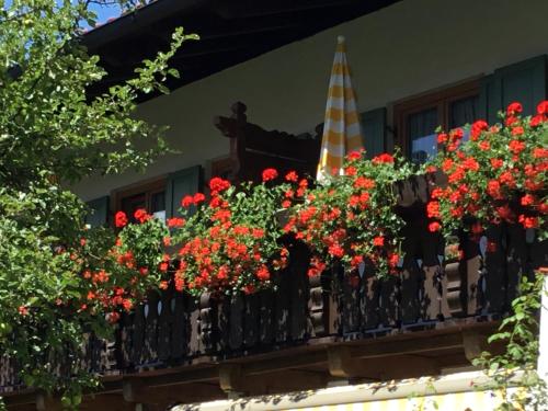 a balcony with red flowers and a spire at Almroeserl in Mittenwald