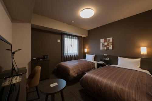鹿嶋市にあるホテルルートイン鹿嶋のベッド2台とテーブルが備わるホテルルームです。