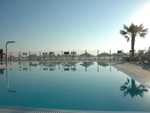 una gran piscina con sillas y una palmera en Hotel Roland, en Riccione