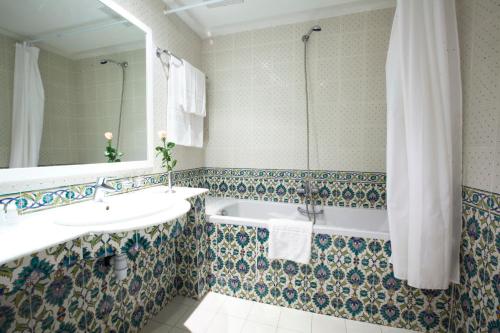 a bathroom with a tub and a sink and a mirror at El Mouradi Cap Mahdia in Mahdia