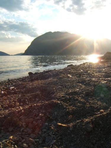 a rocky beach with the sun shining on the water at La Foresta Monteisola in Monte Isola
