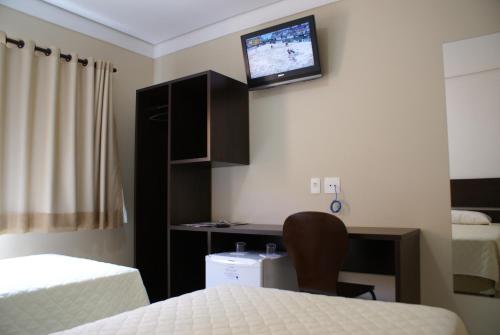 a room with two beds and a desk with a tv on the wall at Cristal Palace Inn in Lins