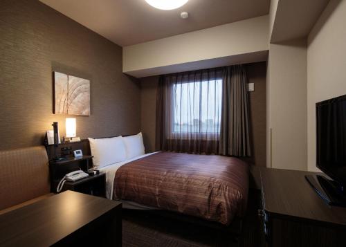 a hotel room with a bed and a window at Hotel Route-Inn Takaoka Ekimae in Takaoka