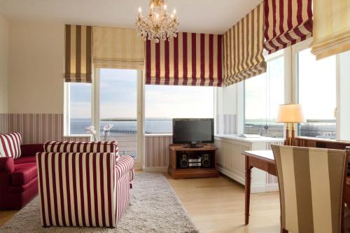 a living room with a couch and a tv and windows at ATLANTIC Grand Hotel Travemünde in Travemünde