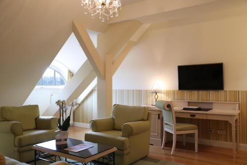 a living room with a couch and a desk and a tv at ATLANTIC Grand Hotel Travemünde in Travemünde