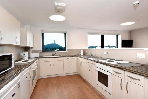a large kitchen with white cabinets and two windows at Juniper Court in Stirling