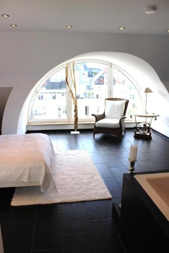 a bedroom with a bed and a chair and a large window at A-Partments in Cologne
